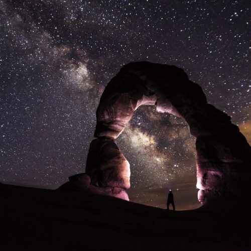 person standing under a rock formation on a starry night